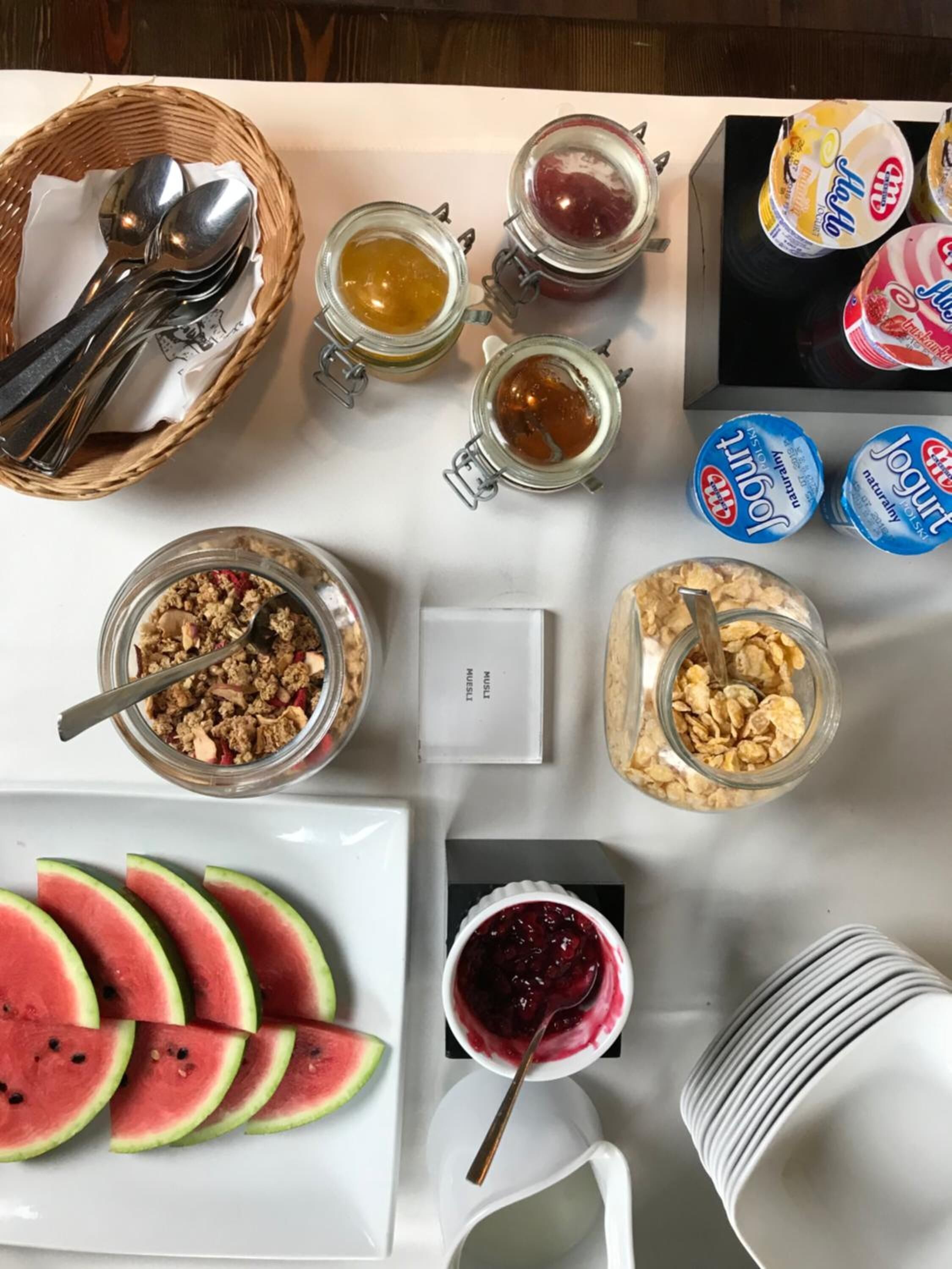 Un bufé de desayuno con diversas opciones de comida, incluyendo yogur, granola y rebanadas de sandía.