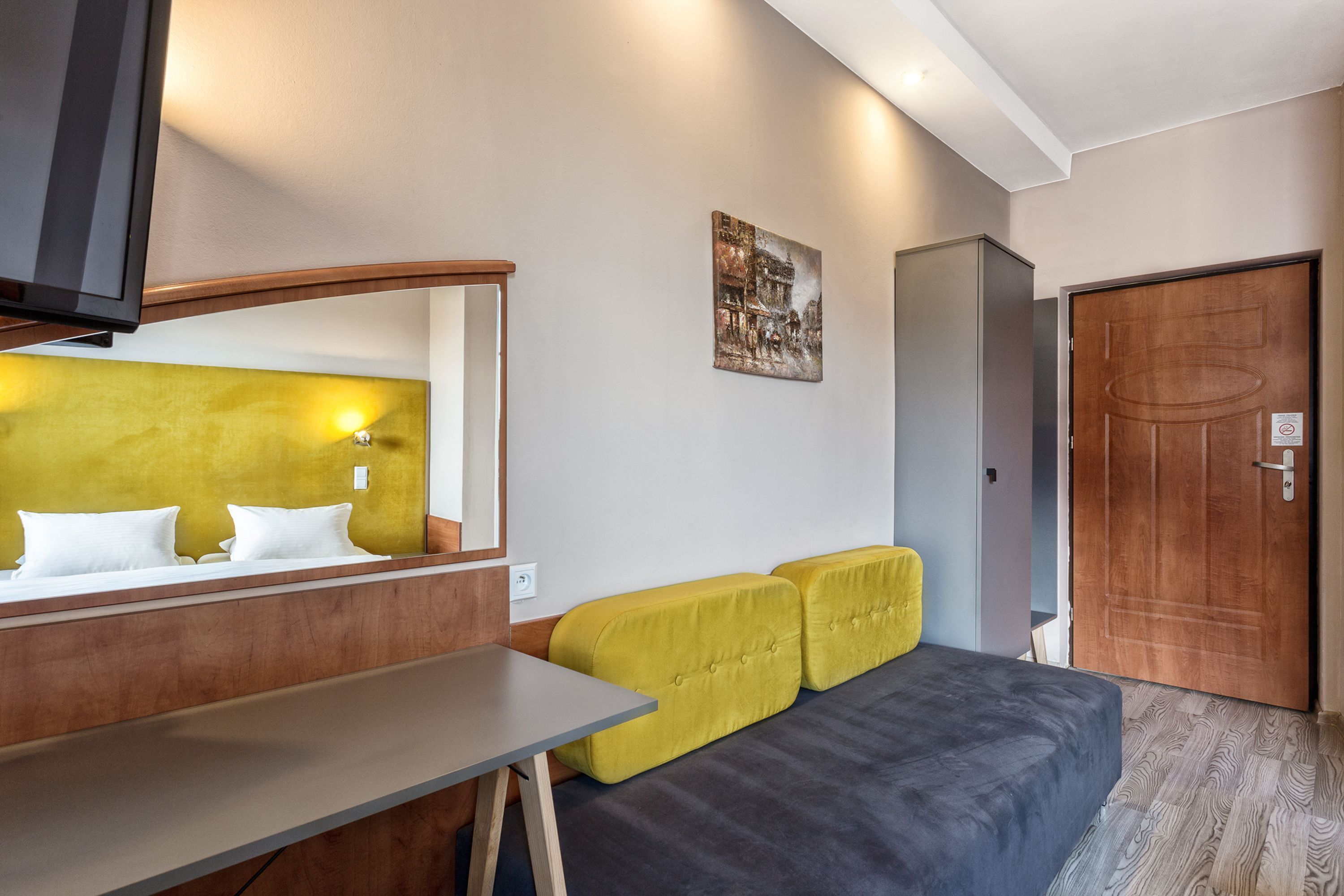 A hotel room with a bed, a small table, a mirror, a television, and a door.
