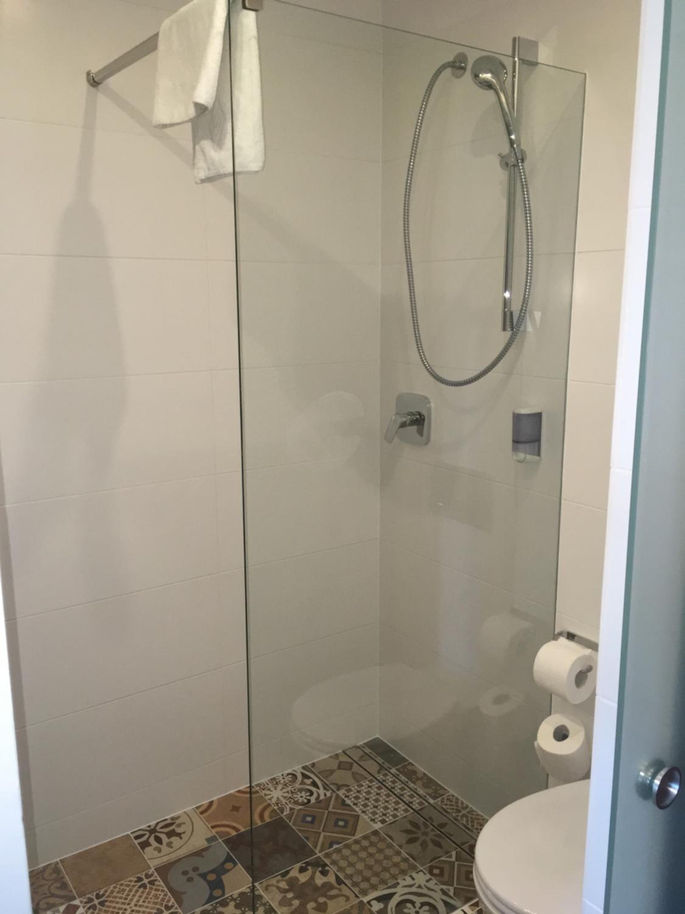 Een douche met glazen wand, een handdouche en een handdoekhouder.