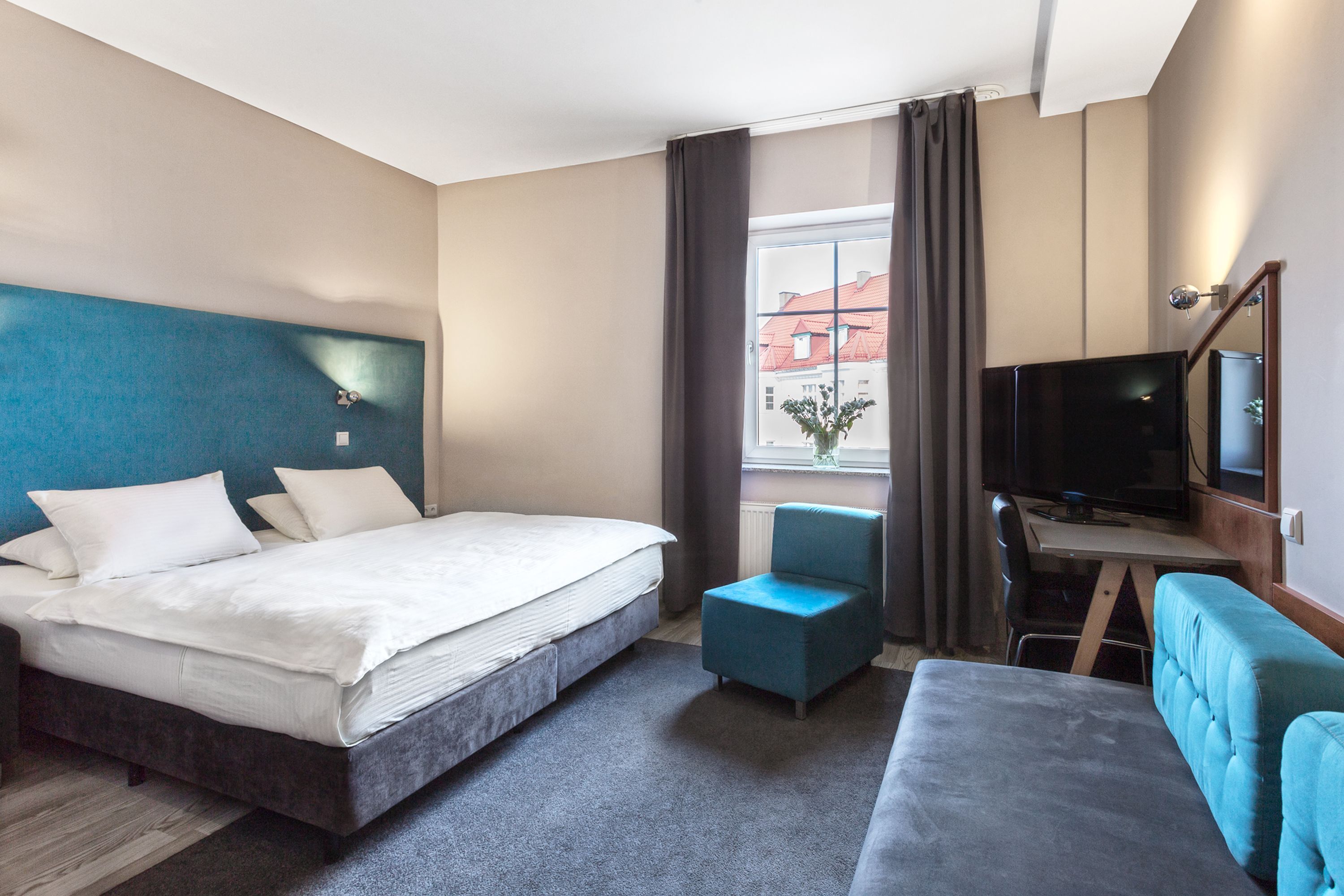 Una habitación de hotel con cama, escritorio con televisor, silla y sofá.