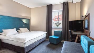 Una habitación de hotel con cama, escritorio con televisor, silla y sofá.