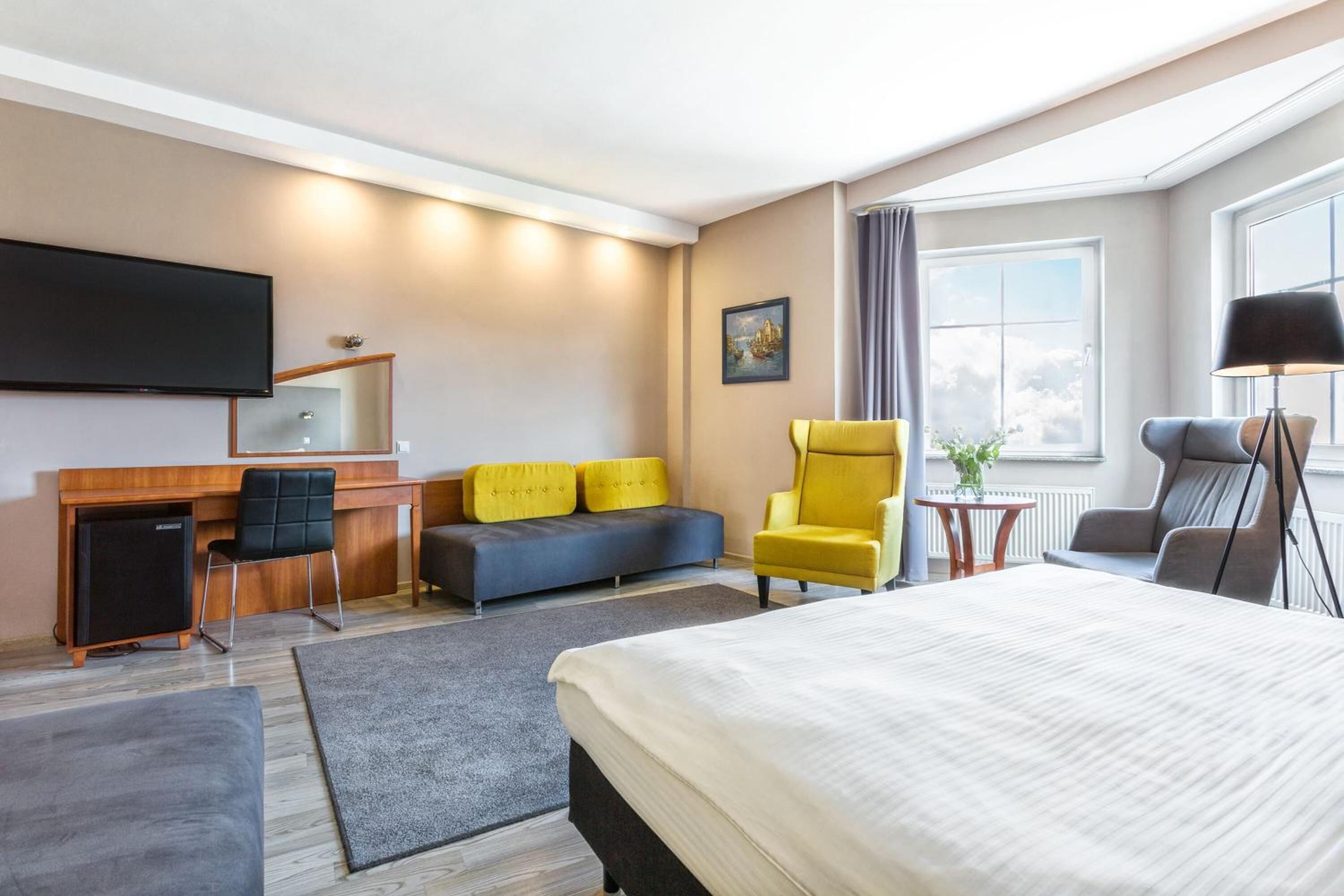 Una habitación de hotel con cama, escritorio, computadora, televisor, sofá y una silla.