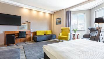 Una habitación de hotel con cama, escritorio, computadora, televisor, sofá y una silla.