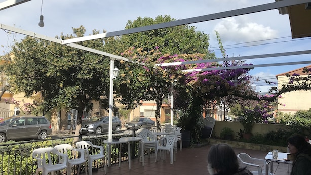 Un espace extérieur aménagé en terrasse, avec des chaises et des tables en plastique blanc, entouré de verdure et de plantes en fleurs.