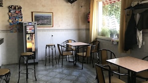 L’intérieur d’un restaurant avec un sol carrelé, de nombreuses tables et chaises, un distributeur automatique, un extincteur et une fenêtre donnant sur un espace verdoyant.