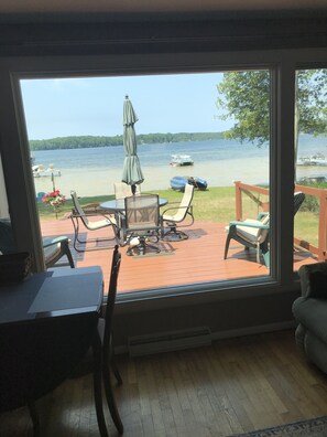 A room with a large window overlooking a deck with outdoor furniture and a view of the lake. - Waterfront Cottage, Lake Ann,Traverse area All Sports Lake! (Lake Ann)