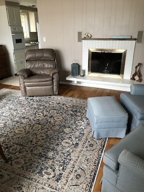 A living room with a patterned rug, a leather chair, a blue ottoman, and a fireplace.