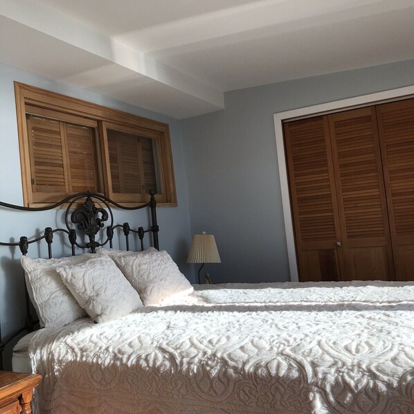 A bedroom with a bed, wooden shutters, a lamp, and a wardrobe. - Waterfront Cottage, Lake Ann,Traverse area All Sports Lake! (Lake Ann)