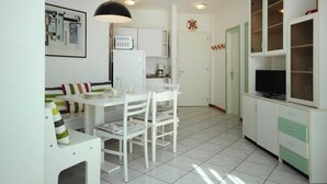 A compact kitchen with white cabinets, a white dining table, and chairs. There is a small refrigerator, a microwave, and a coffee maker. - Apartments Bianco Nero, Lignano Sabbiadoro (Lignano Sabbiadoro)