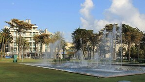 A fountain in a park with palm trees and a building in the background. - Apartments Bianco Nero, Lignano Sabbiadoro (Lignano Sabbiadoro)