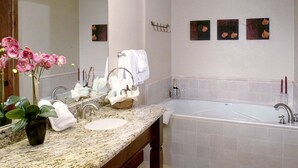 Un baño con encimera de granito, un lavamanos, un espejo grande, una bañera y tres cuadros colgados en la pared.