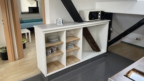 A compact kitchen with a microwave, shelves with dishes, and a small table. - Bed4you Gästehaus 1 (Fuldabruck)