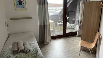 A hotel room with a bed, a chair, a wooden wardrobe, a balcony with a view, and a painting on the wall.