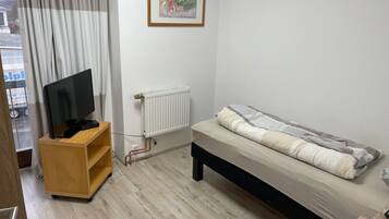 Una camera da letto con un letto, una TV su un mobile in legno, un termosifone e una finestra con tende.
