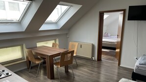 A modern room with a wooden dining table, four chairs, a bed, a TV, and skylights. - Bed4you Gästehaus 1 (Fuldabruck)