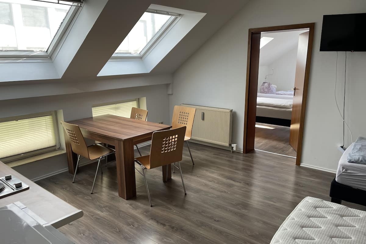 Una habitación moderna con una mesa de comedor de madera, cuatro sillas, una cama, un televisor y tragaluces.