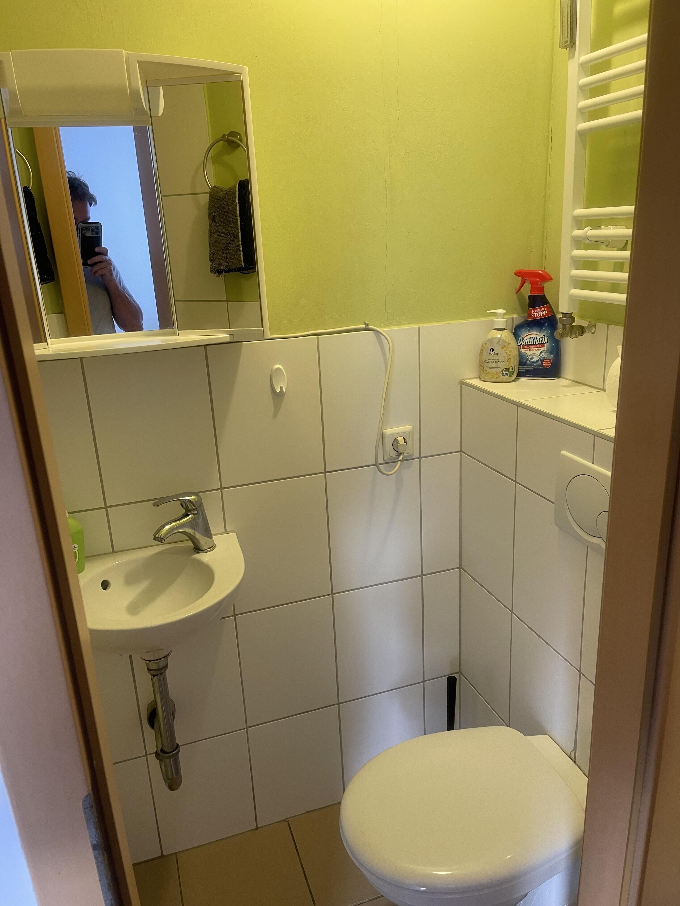 A small bathroom with a white sink, a toilet, and a mirror above the sink. There are two bottles of hand soap and a spray bottle on the counter.