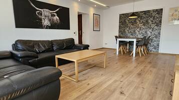 Un salon moderne avec un canapé en cuir noir, une table basse en bois, une table à manger avec des chaises, et une œuvre d’art abstraite en noir et blanc accrochée au mur.