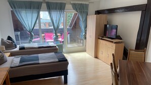 A room with two beds, a wooden table, a TV, and a view of the outside. - Bed4you Gästehaus 1 (Fuldabruck)