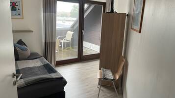 A bedroom with a bed, a chair, a wooden wardrobe, and a sliding glass door to a balcony.