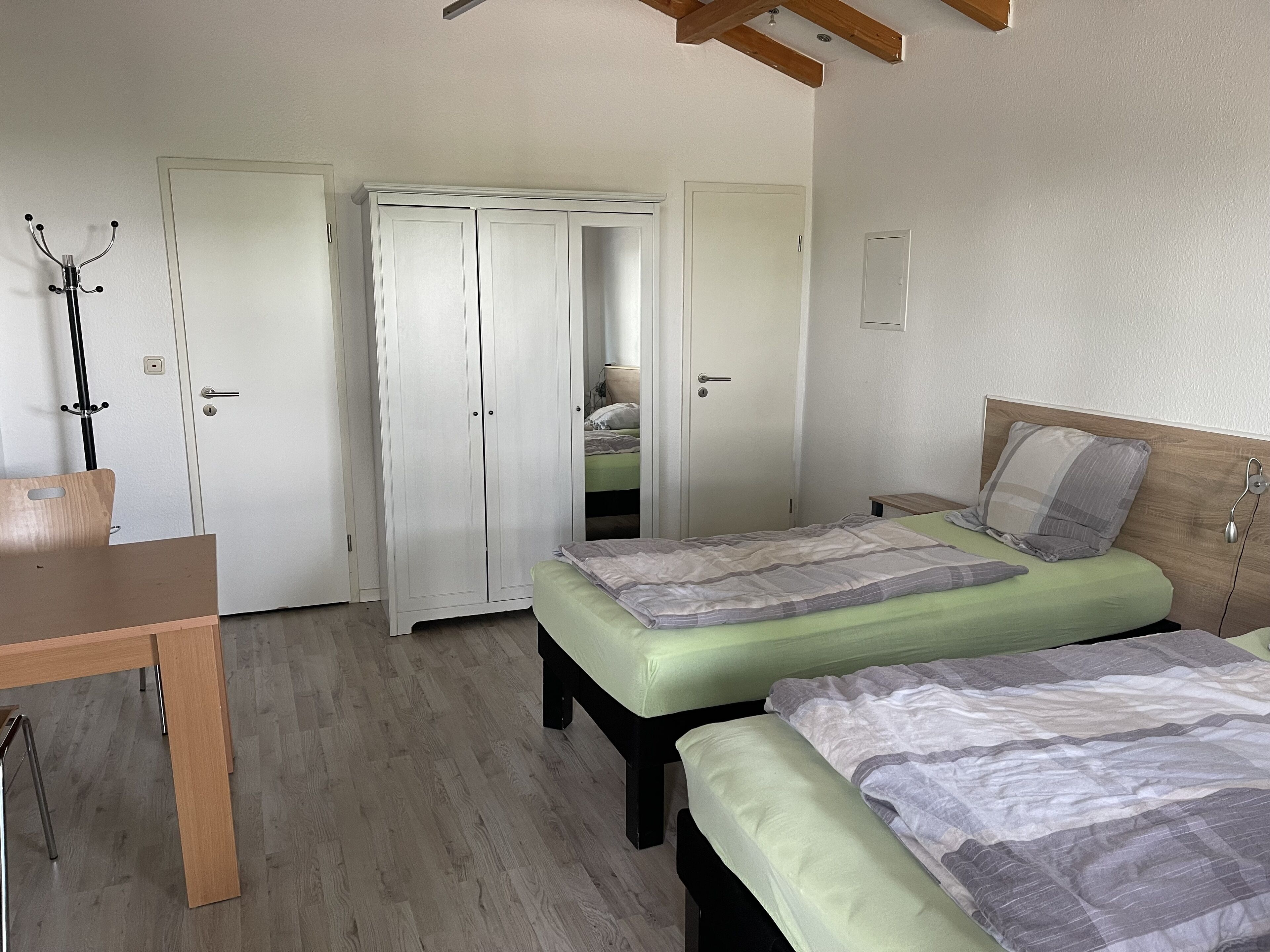 A bedroom with two beds, a wooden desk, and a wardrobe with a mirror.