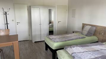 A bedroom with two beds, a wooden desk, and a wardrobe with a mirror.