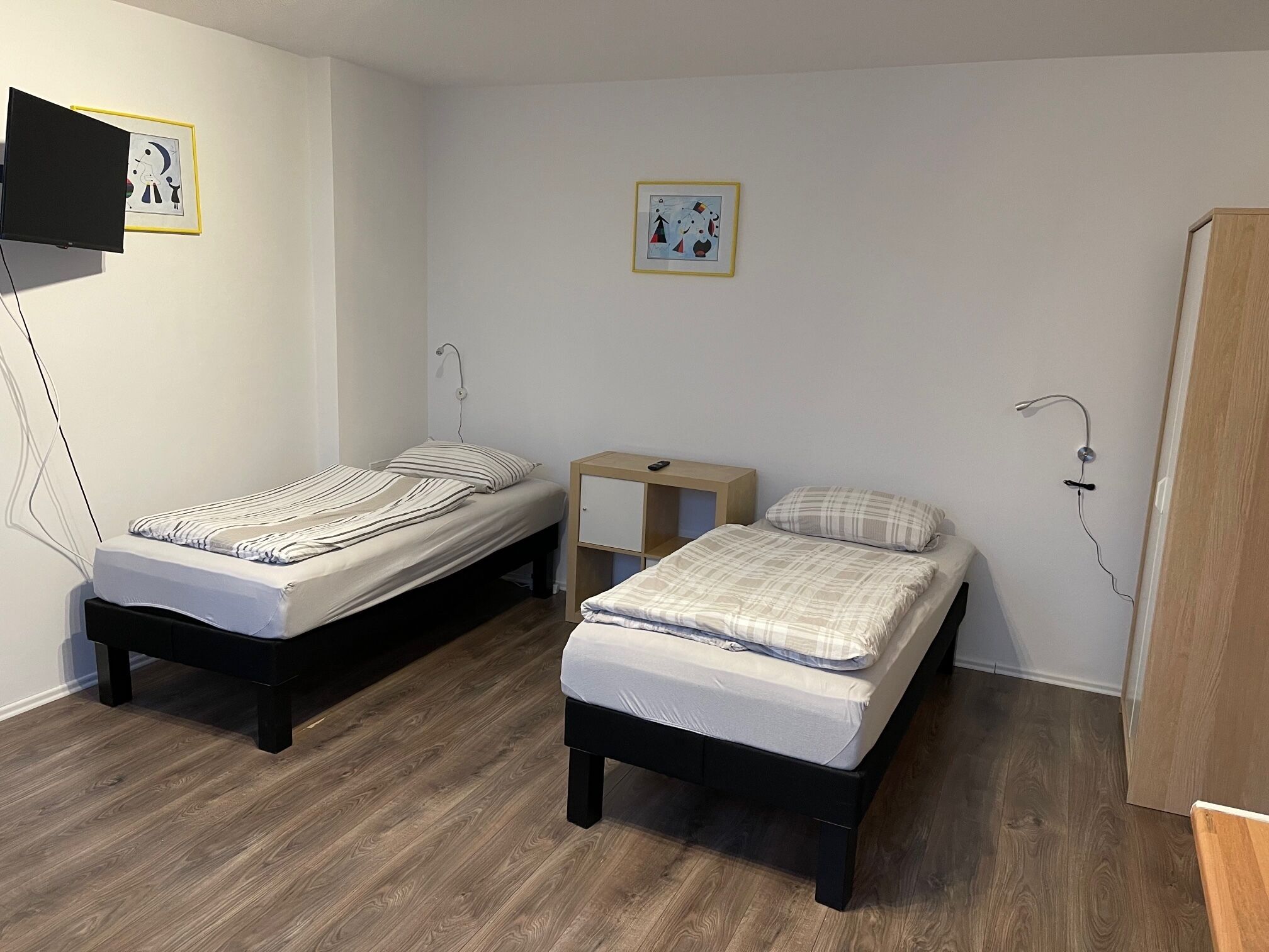 A room with two single beds, a wooden nightstand, a desk, and a wardrobe.