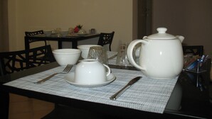 Une table à manger dressée avec de la vaisselle blanche, une théière et des couverts.