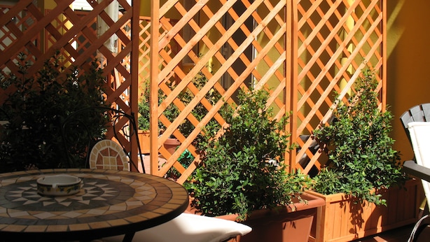 Un espace patio comprenant une table ronde, deux plantes en pot et une cloison en treillis de bois.