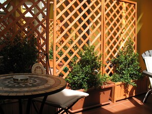 Un espace patio comprenant une table ronde, deux plantes en pot et une cloison en treillis de bois.