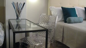 Une chambre d’hôtel avec une table en verre, une chaise transparente et un lit agrémenté d’oreillers blancs et turquoise.