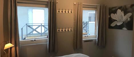 A bedroom with two windows, a bed with a plaid blanket, a bedside lamp, and a wall-mounted coat rack.