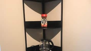 A black corner shelf with three levels, holding a jar of honey, a glass coffee pot, and a yellow box.