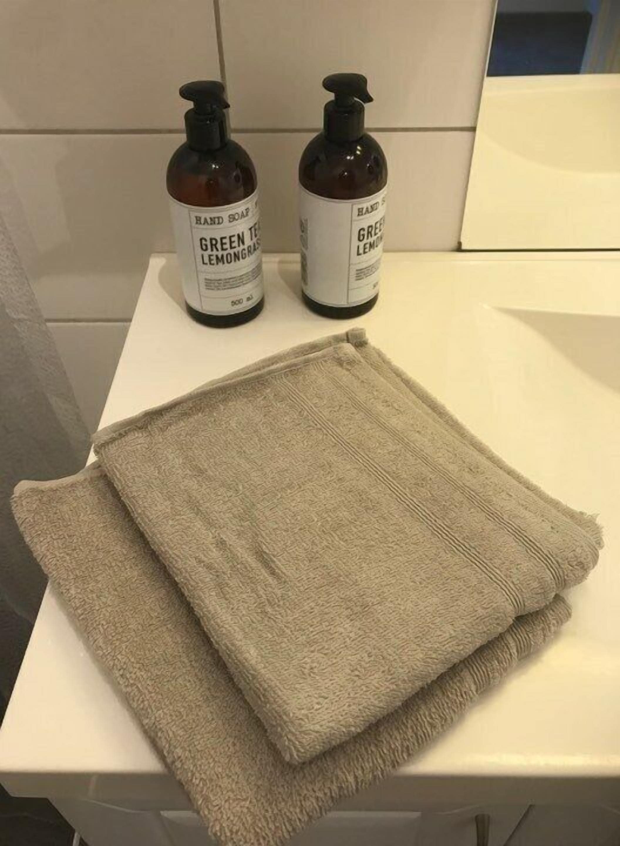 Two bottles of hand soap and a folded towel on a white surface.