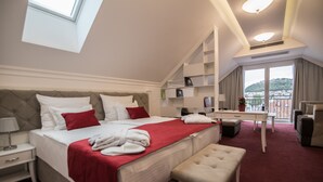 A hotel room with a large bed, a desk, a chair, and a balcony with a view. - Hotel Central Park (Trebinje)