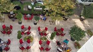 An outdoor café with multiple tables and chairs, surrounded by potted plants and trees. - Hotel Central Park (Trebinje)
