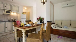 A compact kitchen with a dining area, a sofa, and wicker chairs. - Solenzara Garden Bungalow Retreat (Solenzara)