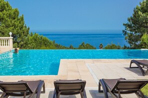 Une piscine avec des chaises longues, une vue dégagée sur l’océan et une terrasse carrelée.