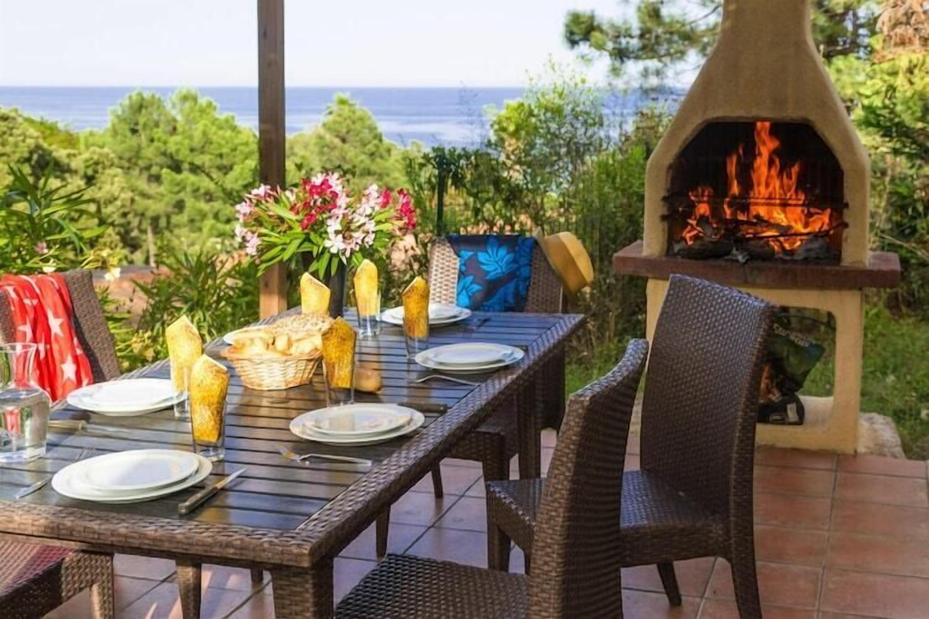 Un'area pranzo all'aperto con un tavolo apparecchiato per due, un braciere e vista sull'oceano.