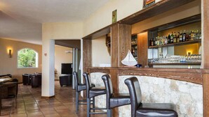 A bar area with a stone wall, wooden bar counter, and several leather bar stools. - Solenzara Garden Bungalow Retreat (Solenzara)