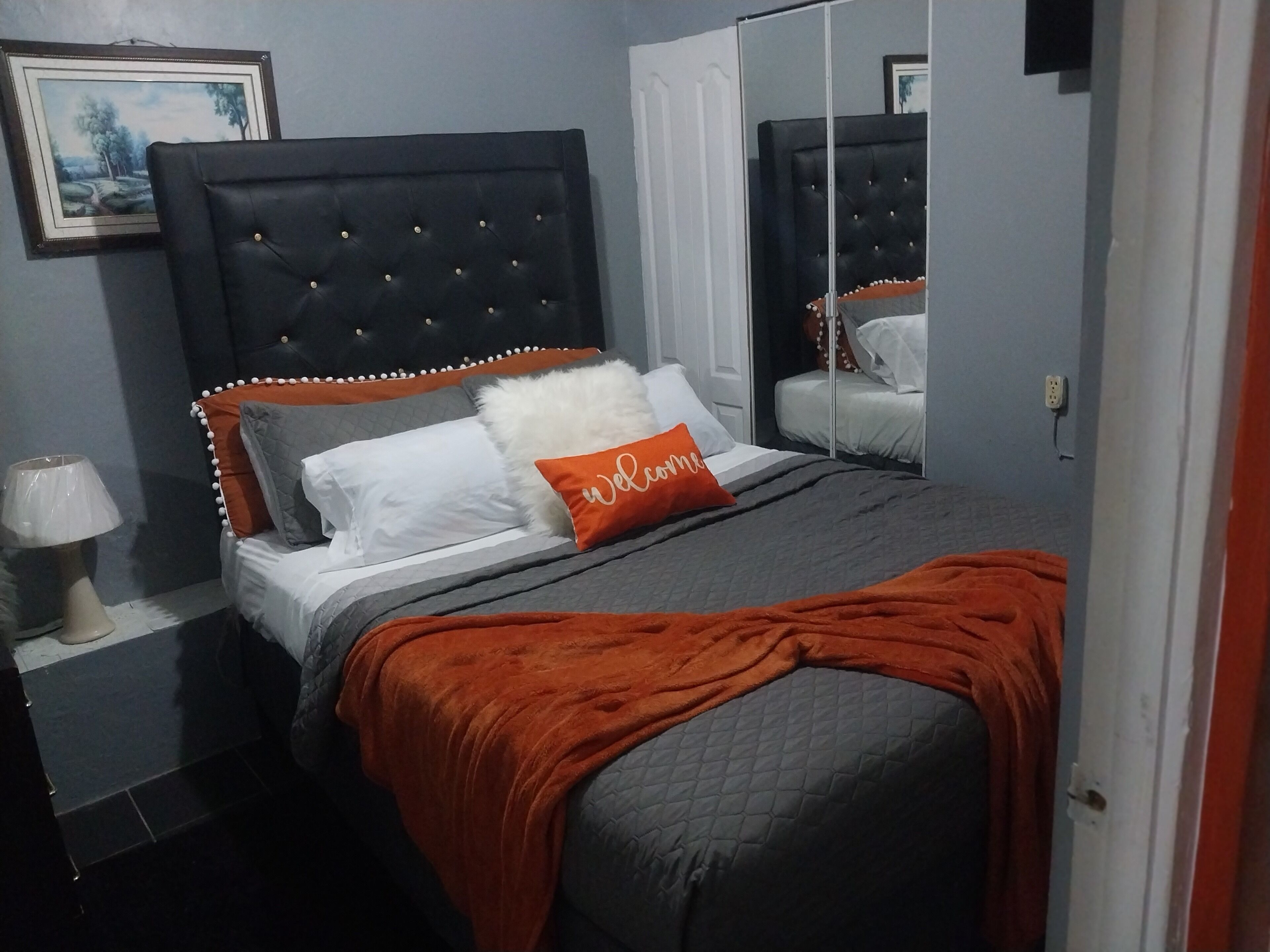 Ein Schlafzimmer mit einem großen Bett, einem Kopfteil, einem Nachttisch mit Lampe und einem Spiegel.