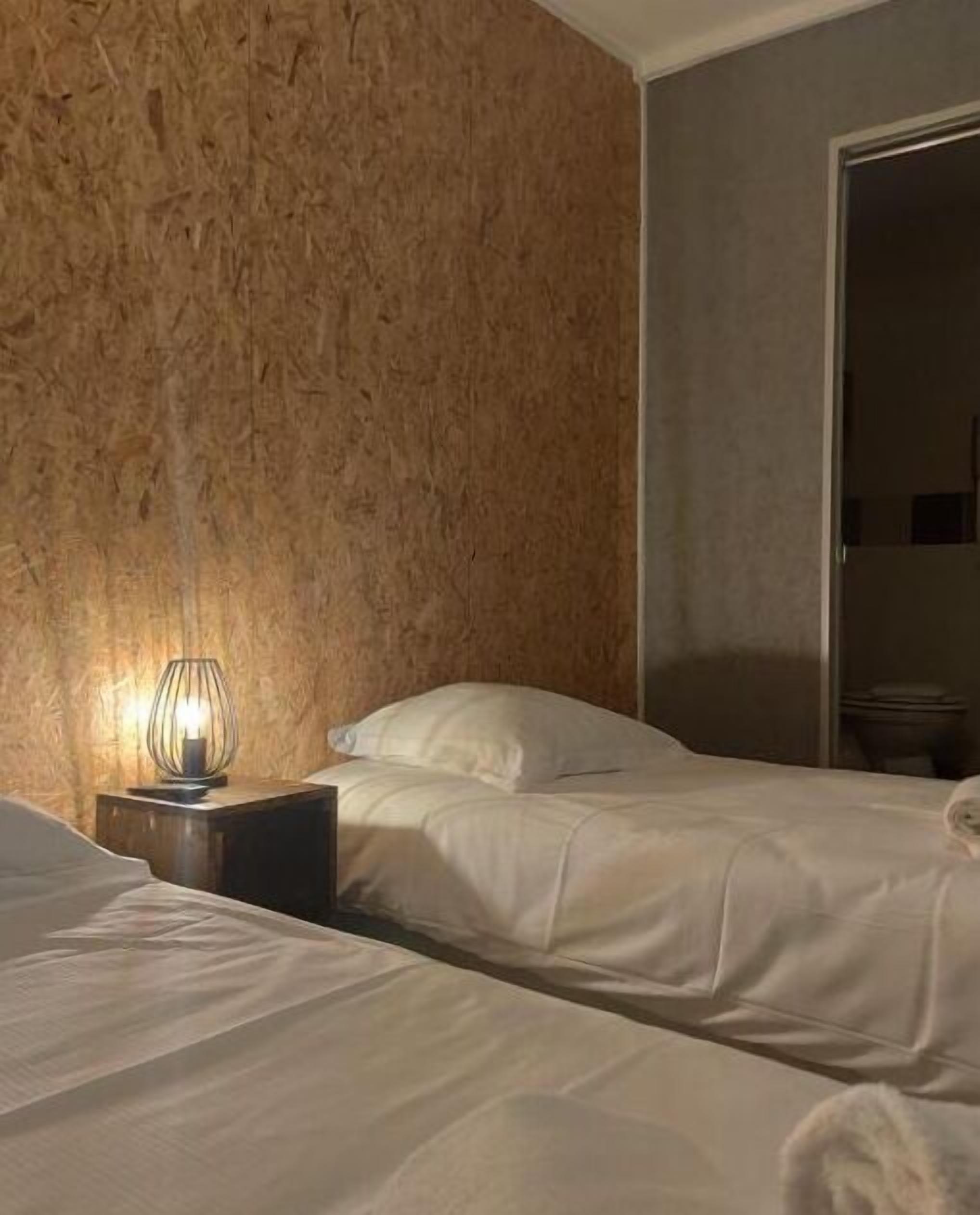 Une chambre avec deux lits, une table de chevet avec une lampe et une porte donnant sur une salle de bain.