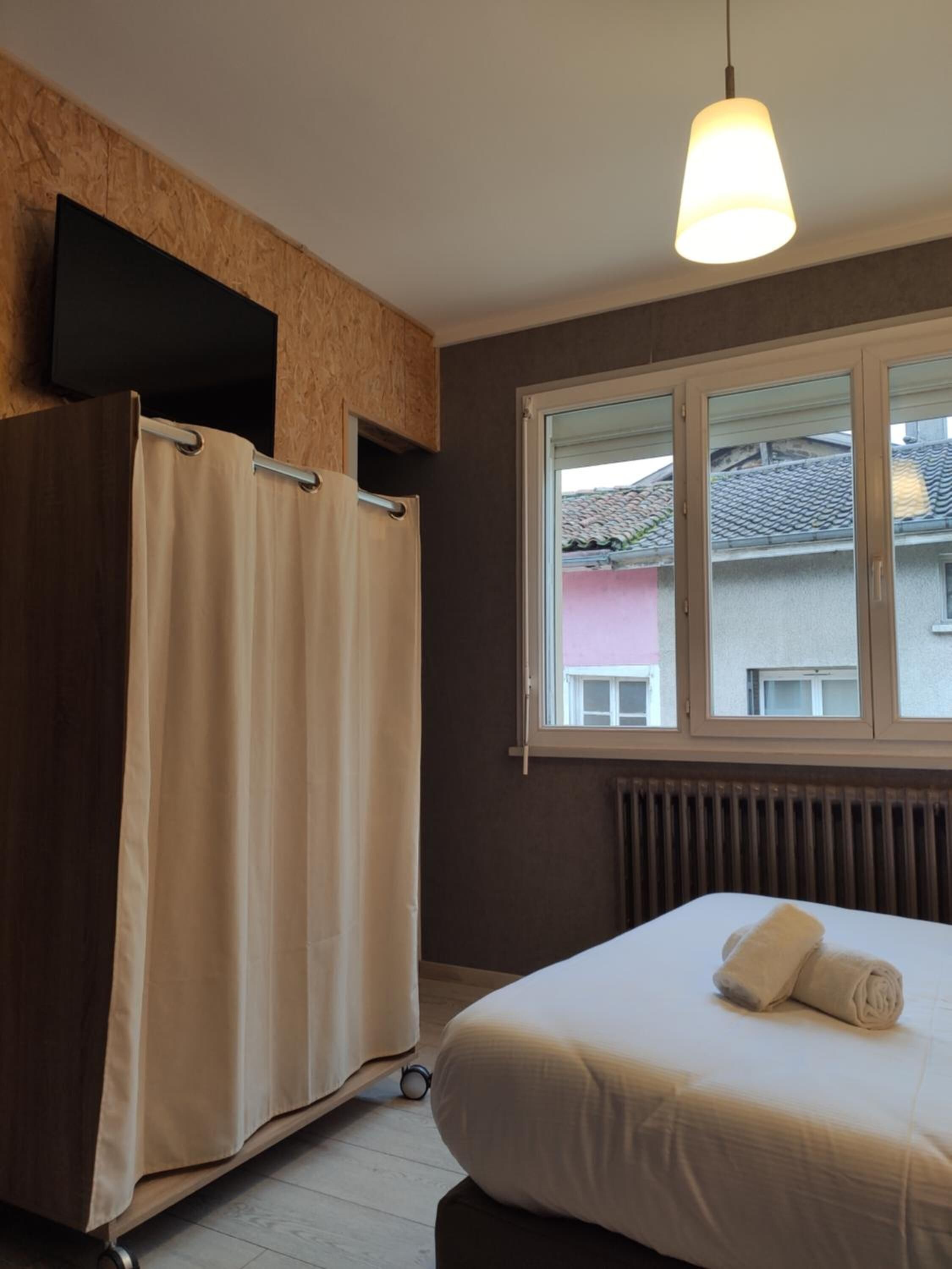 A bedroom with a bed, a window, a radiator, and a curtain.