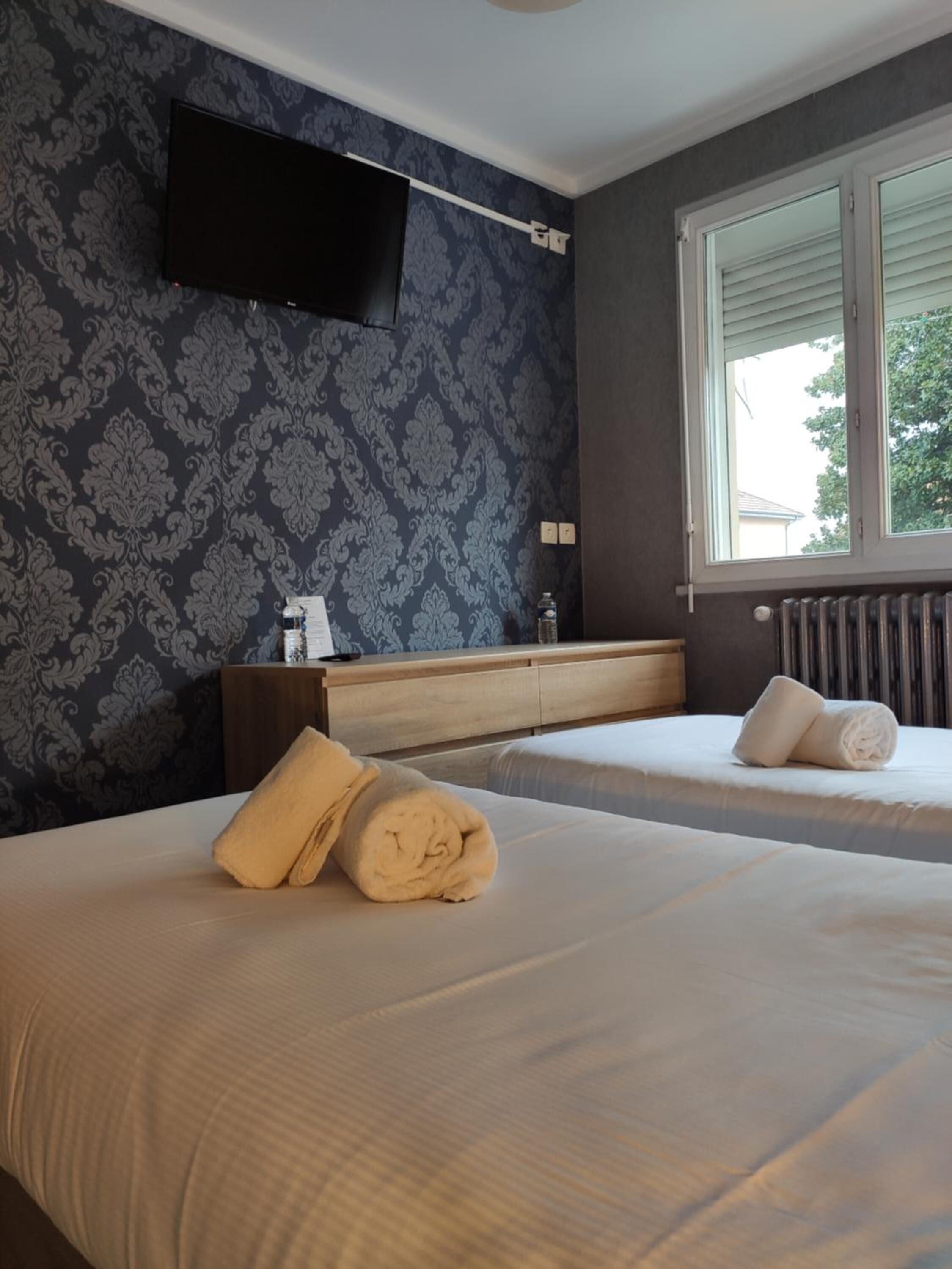 A hotel room with two beds, a flat-screen TV mounted on the wall, a window with blinds, and a radiator.