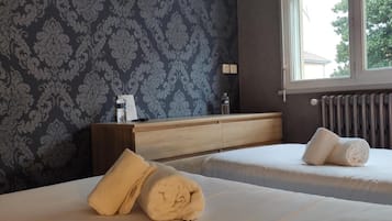 A hotel room with two beds, a flat-screen TV mounted on the wall, a window with blinds, and a radiator.