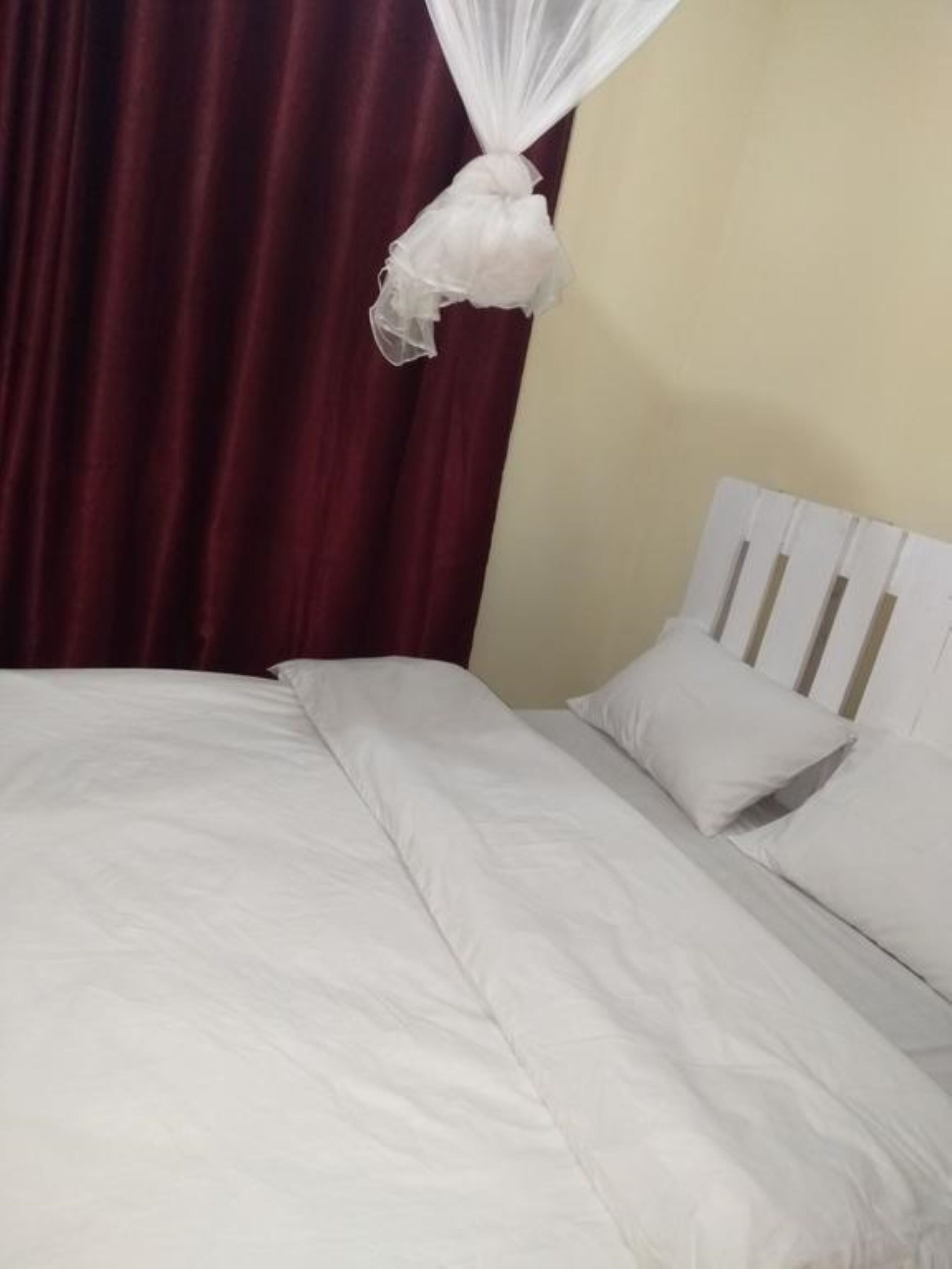 A bed with white bedding and a white headboard, a red curtain, and a white mosquito net hanging above the bed.