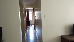 A narrow hallway with a wooden door at the end, a trash bin, and a small table. - Memo's Homestay (Mlolongo)