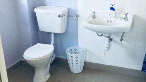 A small bathroom with a toilet, a sink, and a mirror. - Memo's Homestay (Mlolongo)