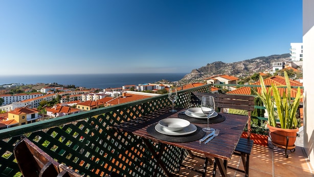 Un balcón con una mesa dispuesta para dos personas, con vista a un pueblo costero y al mar.
