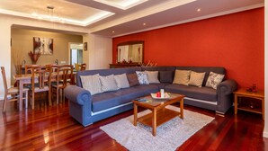 A modern living room with a grey sofa, wooden coffee table, and a dining area with a wooden table and chairs. - Casa Branca II (Funchal)